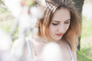 Portrait of young woman in the flowered garden in the springtime. Tender and beautiful posing.