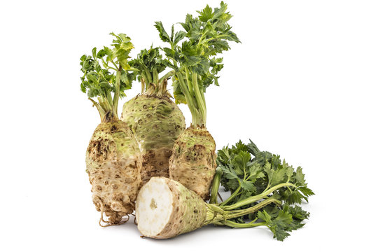 Three fresh organic celery roots with leaves and one cutted on a white background
