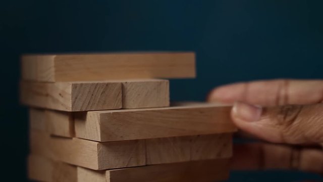 Closeup hand girl take one block on the tower from wooden blocks, dark tone.