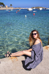Attractive young woman sitting by the sea over the clear water