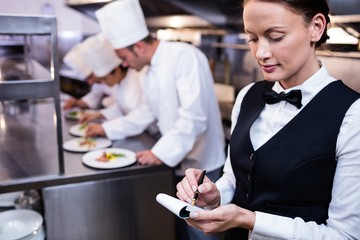 Waitress with note pad in commercial kitchen - Powered by Adobe