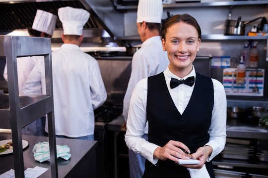 Smiling waitress with note pad in kitchen
