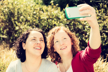 Two sisters are using their mobile Phone to take a selfie outdoors in a Sunny garden.