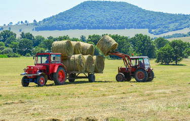 Tractor on field in countryside harvesting straw bales in autumn season 