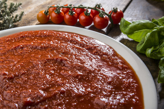 Piatto di sugo con ingredienti quali pomodorini e basilico su tavolo di legno