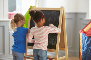 Two Girls Drawing Picture On Blackboard At Home