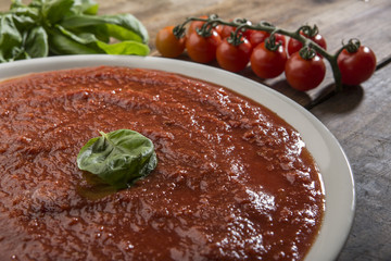 Dettaglio di piatto in porcellana con sugo con ingredienti quali pomodorini e basilico su tavolo di...