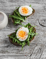 Sandwich with arugula and boiled egg on a wooden board. Healthy breakfast or snack