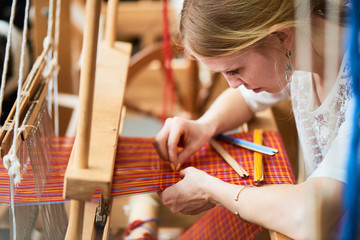 The girl in the production process of textiles are handmade on a loom - obrazy, fototapety, plakaty