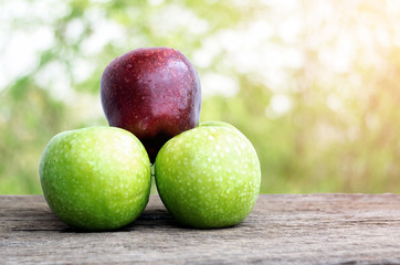 Red apple and green apple on wooden floor with beautiful nature background.
