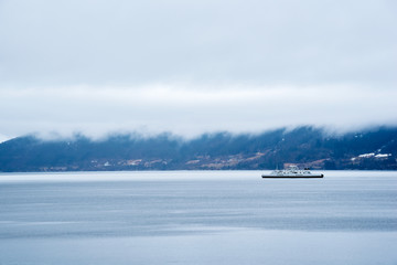 Car ferry in norwegian fjord with low heavy clouds