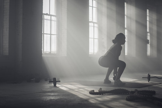 Black woman lifting weights in dark gym