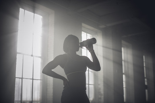 Black woman drinking water bottle in dark gym