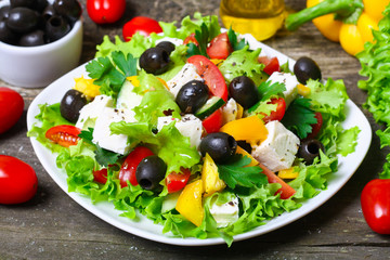 Greek salad with fresh vegetables, feta cheese and black olives on a wooden background