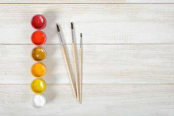 Top view of paint brushes and with colorful gouache containers on wooden background.