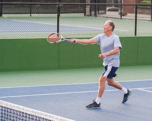 Senior age man showing perfect follow through on running volley. 