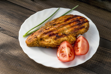 grilled healthy chicken breast served with tomato and fresh chive on white plate on wooden table