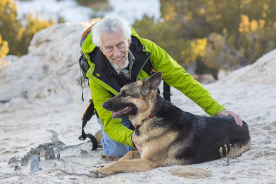 Older Man Petting Dog On Rocky Hillside