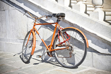 Fototapeta na wymiar Old rusty orange bicycle against a marble wall (Tuscany - Italy)