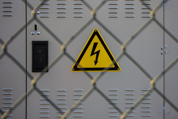 electrical hazard sign placed on a electric power substation behind a metal fence of wire mesh