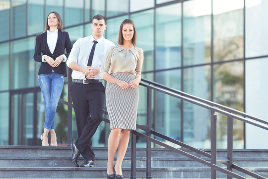 Three young business people on a standing on the stairs in front of the modern office building