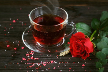 Tea in a transparent cup, color candies and a red rose