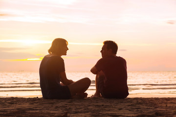 man and woman on the beach at sunset, young couple talking near the sea, dating or friendship concept - Powered by Adobe