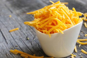 Shredded cheddar cheese in white cup  close up view