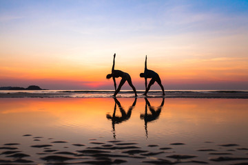 stretchings on the beach at sunset, yoga exercises, silhouettes of couple
