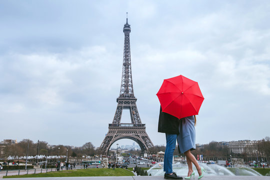 honeymoon in Paris, couple kissing behind red umbrella against Eiffel tower