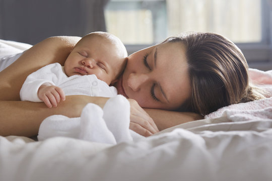 Mother hugging newborn baby on bed