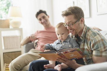 Caucasian gay fathers reading to baby in living room
