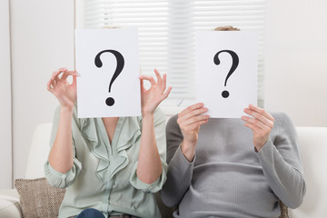 Couple Holding Question Mark Sign In Front Of Face