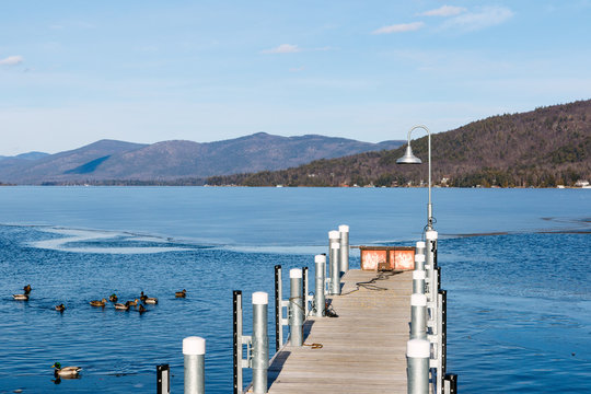 Color DSLR stock image of a frozen Lake George, with metal and wood pier in the foreground and Adirondack Mountains in background. Horizontal with copy space for text
