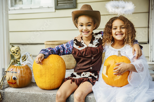 Sisters wearing Halloween costumes with jack-o-lanterns on porch