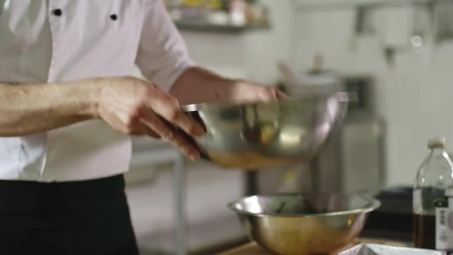 Close up of restaurant chef jumbling up a salad in metal bowl in the kitchen