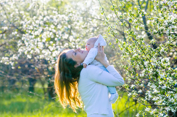 Obraz premium Little baby boy with her young mother in the blossom garden