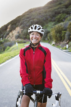 Woman with bicycle smiling on remote mountain road