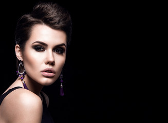 Beauty Fashion Model Girl with short hair. Brunette Model Portrait. Short haircut. Sexy Woman Makeup and Accessories. Isolated on black. Hair cut. Purple Earrings