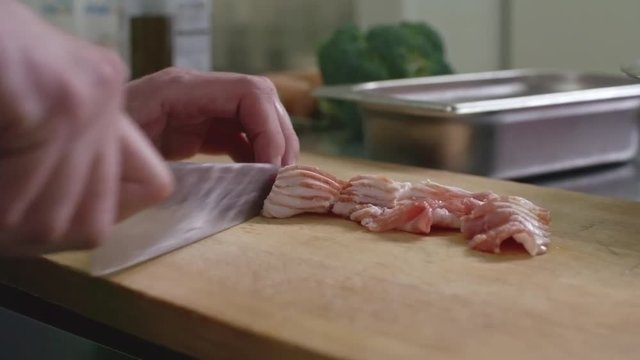 Close up of male hands cutting bacon with knife on wooden board