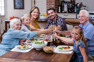 Multi-generation family toasting glass of wine while having meal