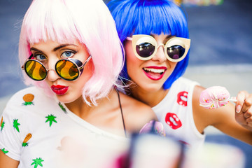 Two bright funny cool fashionable girl in blue and pink wigs, sunglasses, make selfie at an...