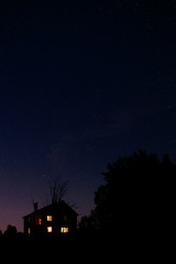 The rural house with the lit windows against the night star sky