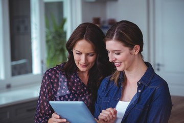 Obraz premium Two beautiful women using digital tablet in kitchen