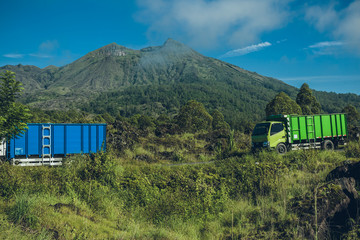 Blue and green trucks arrives on an asphalt road. Mountains in t
