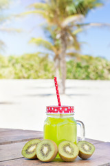 Kiwi juice and kiwi slices on a wooden table at the beach with palm trees