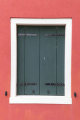 Old window with dark shutters on red wall