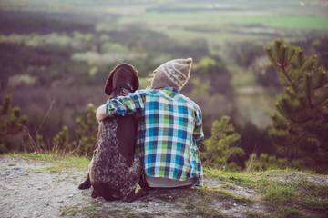 Woman and her dog posing outdoor. Girl loving and hugging tightly her dog and watching landscape.