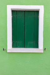 Old window with dark green shutters on light green wall