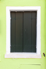 Old window with dark green shutters on light green wall